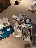 Wide shot of multiple plastic bins and container holding various bead making supplies including strings, beads, tools, wire, and crafting components