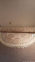 Rolled wool oval carpet showing part of floral design and fringe at the end.