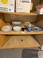 Shelf with an assortment of small decorative plates, a large ornate plate, and two lidded containers in blue and white patterns.