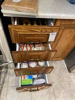Wooden kitchen drawers with some cutlery, utensils, and storage wraps visible.