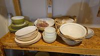 Shelf with assorted bowls, plates, and dishes including green glazed bowls, white ceramic bowls and plates, and some wrapped items