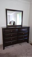 Front view of dark wood dresser with eight drawers and large matching framed mirror hung above.