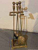 Full view of the antique brass fireplace tool set in the brass stand with visible tarnish and wear.