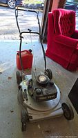 Full view of the Craftsman Eager-1 lawn mower standing on a concrete floor beside a red jerry can and a red armchair in the background.