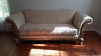 Full front view of the large beige over-stuffed couch with single seat cushion and carved wooden frame details.