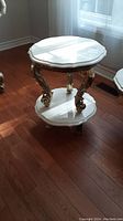 Full view of the marble side table showing the shaped marble top, carved gold-tone legs, and lower marble shelf.