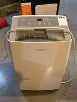 Front angle view of entire white Noma branded dehumidifier unit with power cord wrapped around top.