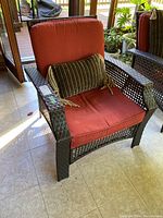 Front view of outdoor chair with red cushion and green decorative pillow on tiled floor by window.