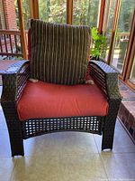 Front view of outdoor wicker chair with orange cushion and striped decorative pillow.