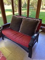 Front view of outdoor loveseat with red cushions and brown accent pillows
