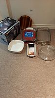 Photo showing Black & Decker rice cooker box, Anchor 4-piece casserole set with lids, wooden salad bowl, white rectangular serving dish, clear glass round casserole dish, clear rectangular glass baking dish, and small white ceramic pan placed on floor.