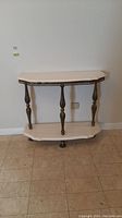 Front view of the half moon side table showing marble top, marble lower shelf and four decorative metal legs.