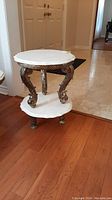 Full view of the marble side table showing the top marble surface and the ornate metal legs connecting to the lower marble shelf.