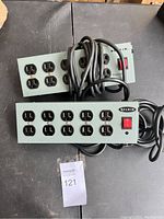 Two gray industrial Belkin power strips side by side on a dark surface, showing power cords and multiple outlets.