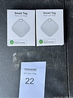 Photo of two sealed white boxes labeled Smart Tag with Apple Find My compatibility logo.