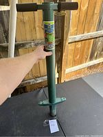 Photo of green metal ProPlugger 5-in-1 planting tool with black handles. Shows label and body of tool.