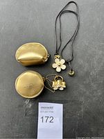 Two gold-tone Marc Jacobs jewelry pouches and a gold-tone flower pendant necklace on black cord.