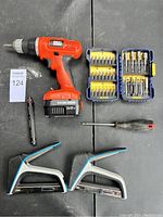 Photo showing Black & Decker cordless drill, two cases of drill bits, screwdriver, two clamps, and a bit holder tool on black surface
