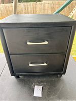 Front view of black leather end table with two drawers and silver handles, sitting outside on a table.