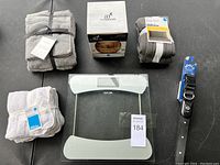Photo shows most of the lot items arranged including towels, a wooden bowl, a glass scale, and a black pet collar.