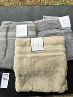 Three folded Threshold Performance bath towels displayed on a dark surface outdoors: two gray and one beige.