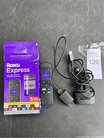 Photo showing Roku Express packaging box, streaming device remote, HDMI cable, and power adapter on a gray surface.