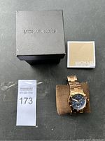 Michael Kors box, paperwork and watch on cushion
