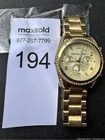 Photo of gold-tone Michael Kors wristwatch alongside MaxSold lot number 194 tag.