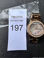 Michael Kors women's watch showing rose gold tone metal, crystal accents around bezel and mother-of-pearl dial with date window.