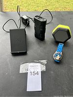 Lot of 4 items: wireless charger, portable battery pack, Bluetooth speaker, Sonic the Hedgehog wristwatch arranged on table