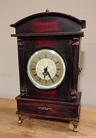Front view of the antique style quartz mantle clock showing clock face with Roman numerals and wooden body with metal accents.