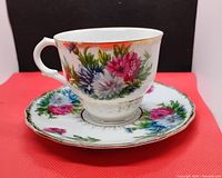 Side view of the tea cup on the saucer showing colorful floral pattern and gold trim on white ceramic.