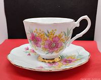 Front view of vintage tea cup and saucer with floral design and gold trim on a red background.