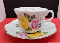 Close-up of tea cup with pink and yellow rose floral pattern and gold rim