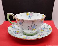 Photo of tea cup and saucer showing floral pattern, gold trim, and scalloped edges on the cup