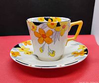 Photo of vintage tea cup and saucer with yellow and orange flowers, showing full cup and most of saucer, against a red and black background.