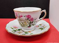 Tea cup and saucer set displayed upright on red background showing floral design and gold trim.