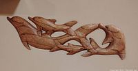 Photo of wooden dolphin family wall art showing six dolphins carved and joined into a single wooden piece, photographed from front to show overall shape and detail.