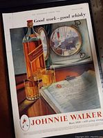 Photo of framed vintage Johnnie Walker whisky advertisement featuring the bottle, two glasses, ledger book, and ship porthole.