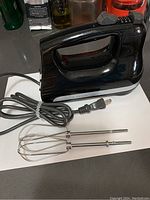Full side view of the black KitchenAid hand mixer showing handle, attached power cord, and one beater inserted.