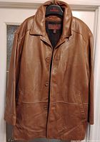 Front view of the men's brown leather jacket on a hanger, showing button closure, collar, and side pockets.