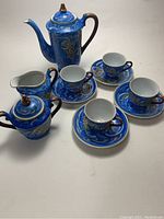 Full set displayed showing teapot, sugar bowl, creamer, four cups and saucers in blue with raised dragon designs.