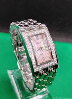 Side angle view of the silver-tone quartz watch showing rectangular face with crystal bezel and linked metal band on a green background.