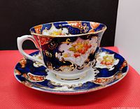 Tea cup and matching saucer on red surface showing detailed exterior ornate floral and gold pattern with cobalt blue background