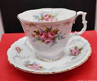 Photo showing the tea cup filled with floral designs of pink roses and blue flowers, scalloped gold trim, and ornate handle.
