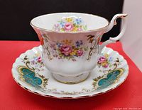 Front side of the tea cup on the saucer, showing floral and gold detailed design with scalloped edges.
