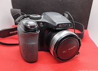 Front and angled side view showing camera body, grip, lens with Fujifilm lens cap and part of the neck strap.