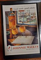 Framed vintage advertisement for Johnnie Walker whisky showing the bottle, two glasses, and scenic window view.