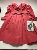 Front view of the pink corduroy dress showing collar, sleeves, and bow detail with attached tag