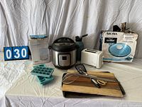 Group shot showing dehumidifier box, Instant Pot, water bottle, toaster, Aroma grill box, ice cube trays, cutting board, utensils and cookie sheet